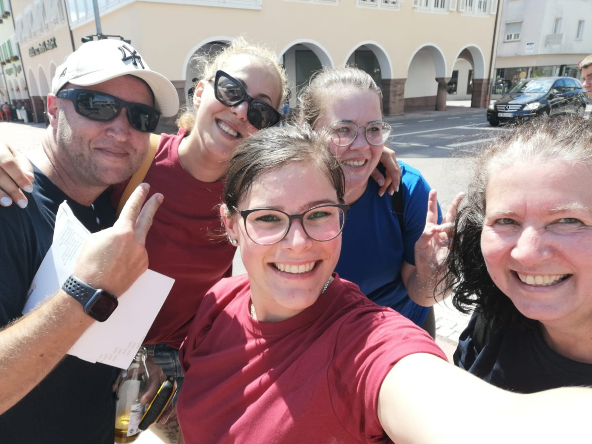 Gruppe von sechs lächelnden Freunden macht ein Selfie im Freien an einem sonnigen Tag.