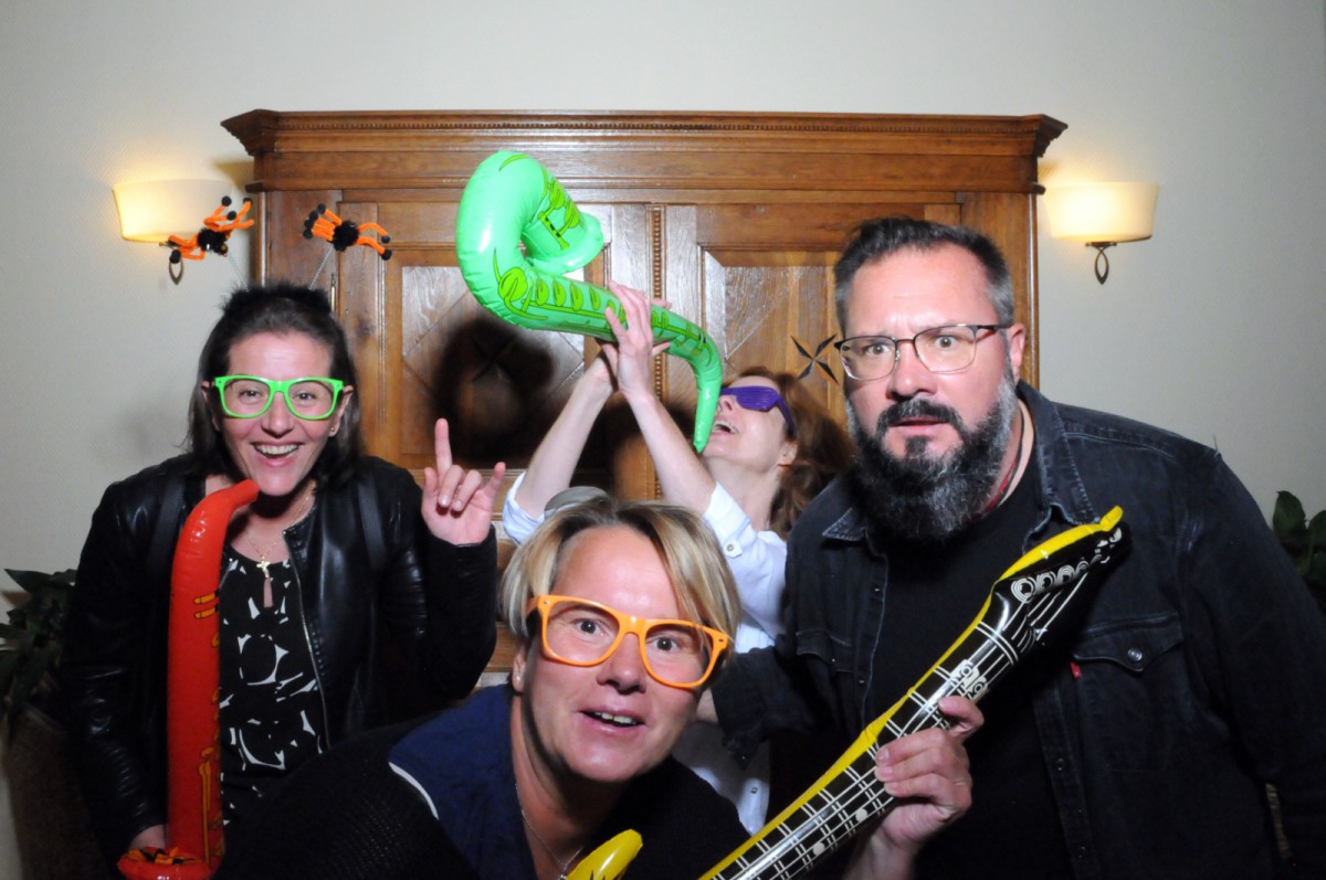 Four people posing with props like an inflatable saxophone, a yellow guitar, and colorful glasses.