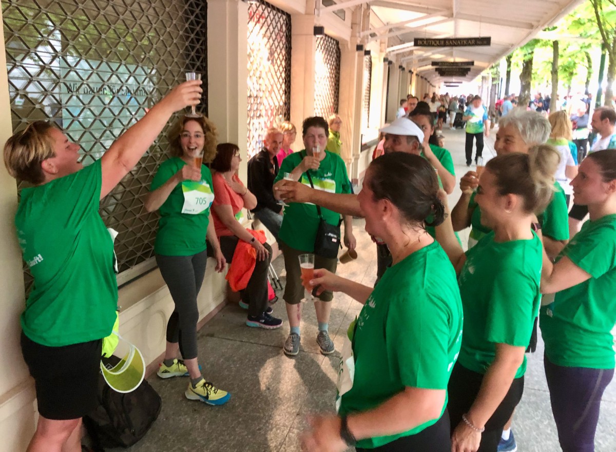 Group of people in green t-shirts interacting and holding drinks.