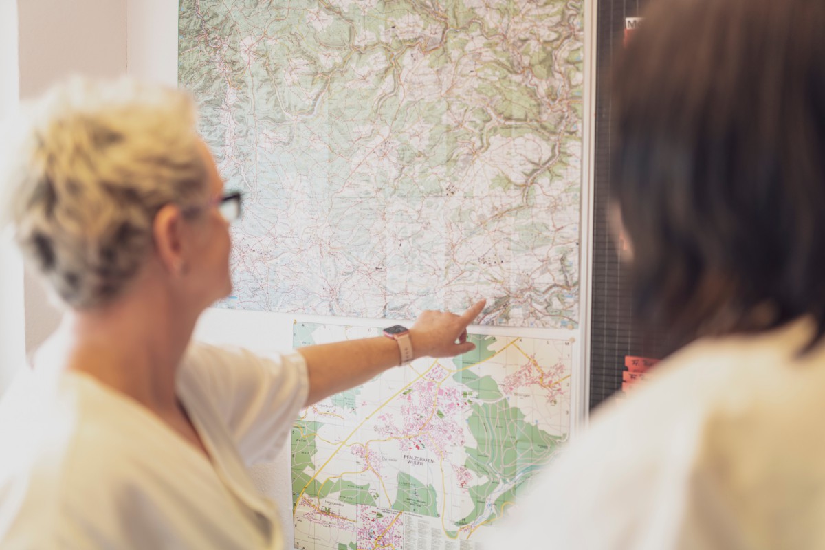 Two people in office attire discussing a large wall map, with one person pointing to a spot on the map.