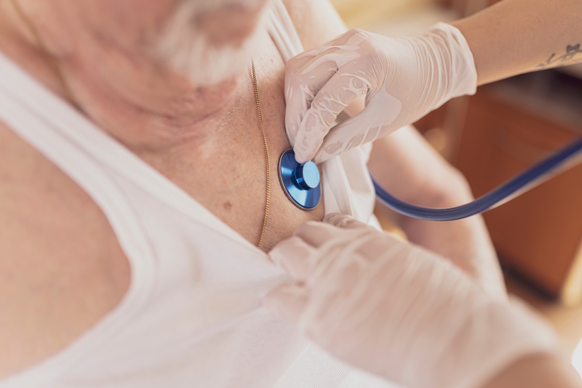 Doctor's gloved hand examining a patient with a blue stethoscope, patient wearing a white top.