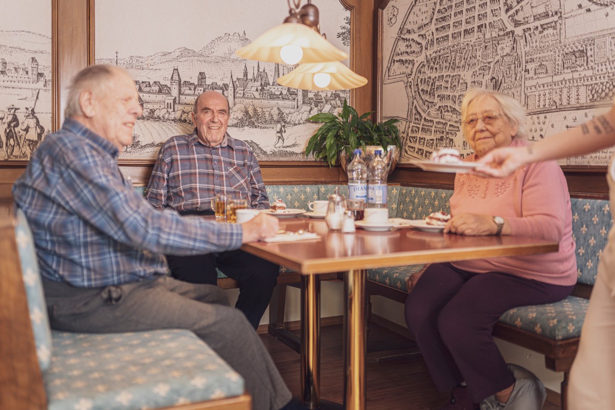 Three elderly people sitting at a table in a cozy cafe with historic wall decor.