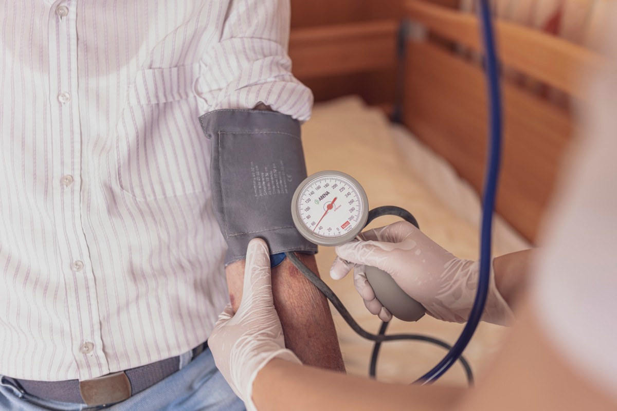 Medical blood pressure measurement with cuff and device. A hand with a white glove places the blood pressure cuff on the arm of a person wearing a striped shirt.