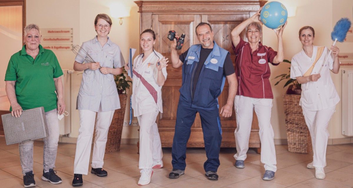 Six employees stand in various work uniforms side by side. A central male figure in dark blue workwear stands confidently in the center of the group.